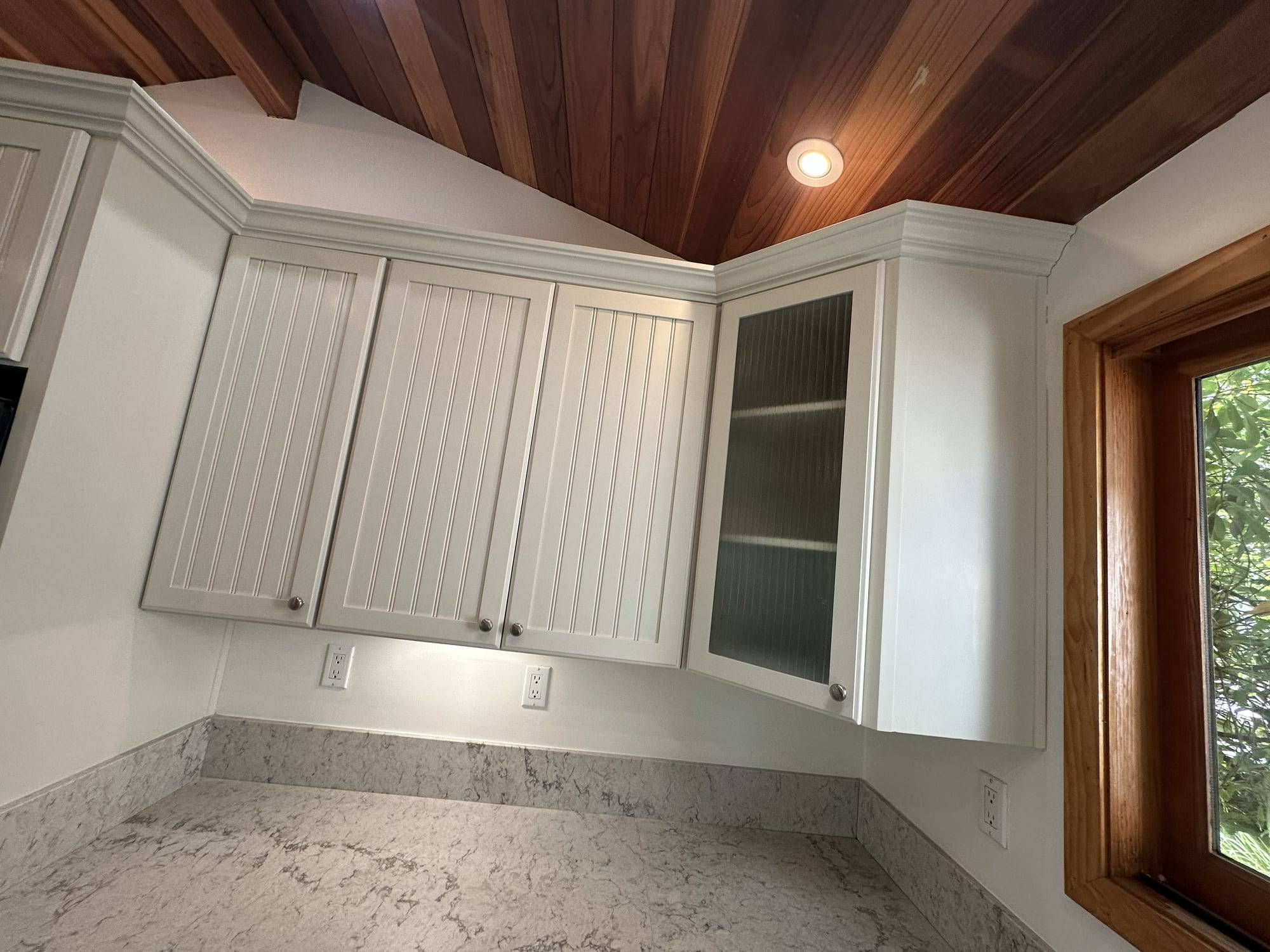 White painted upper cabinets under a wood ceiling
