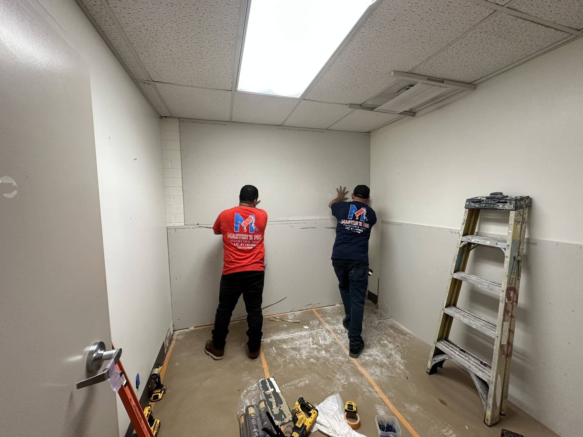 Crew prepping walls in a small commercial room, wide view